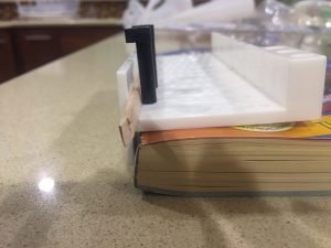 A close up of the miter box on the phone book with the balsa wood strip hanging out of the edge of the miter box